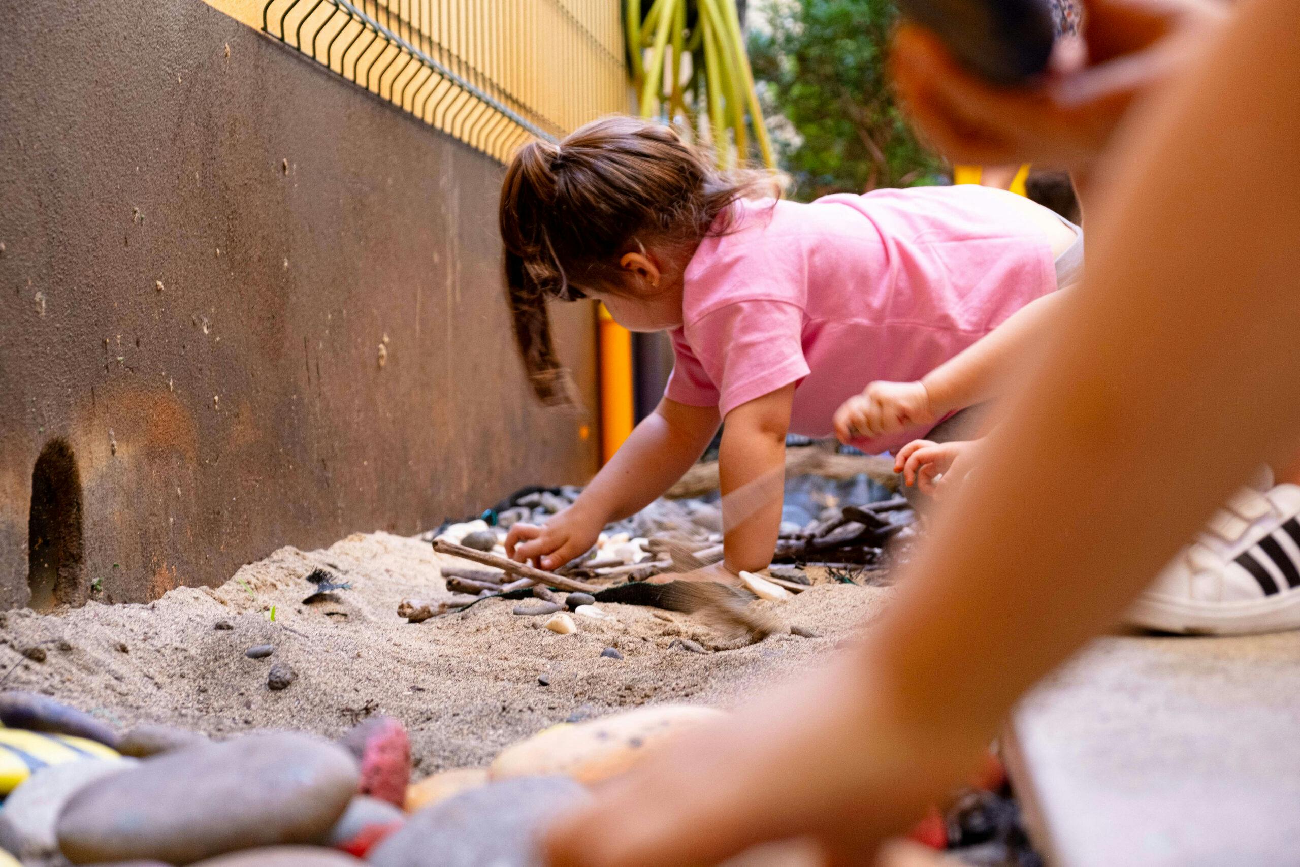 Menina a brincar com materiais de várias texturas, no parque do infantário A Toca dos Traquinas