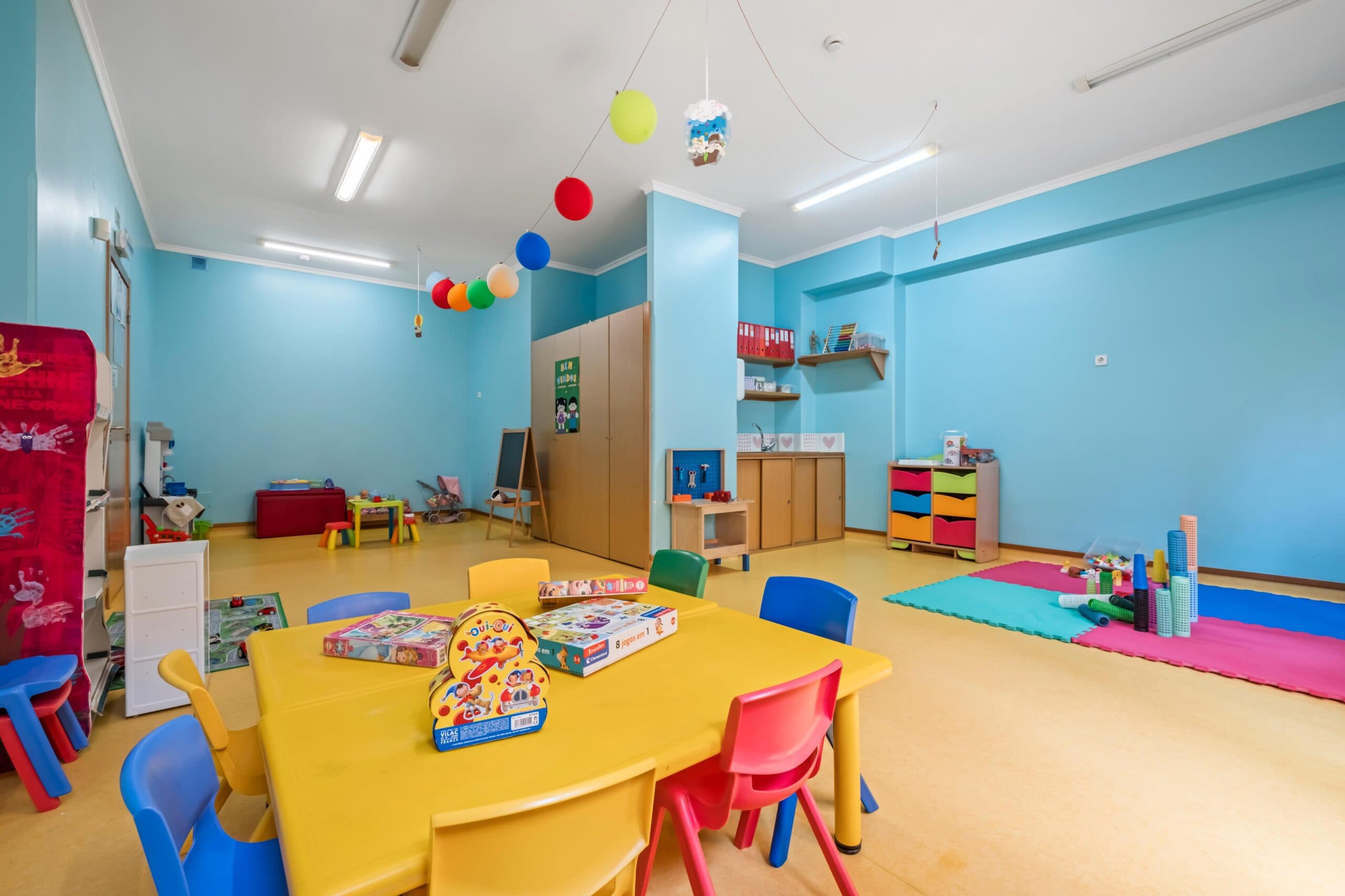 Sala jardim de infância Texugos com mesas, cadeiras, tapete e diversos brinquedos, no infantário A Toca dos Traquinas