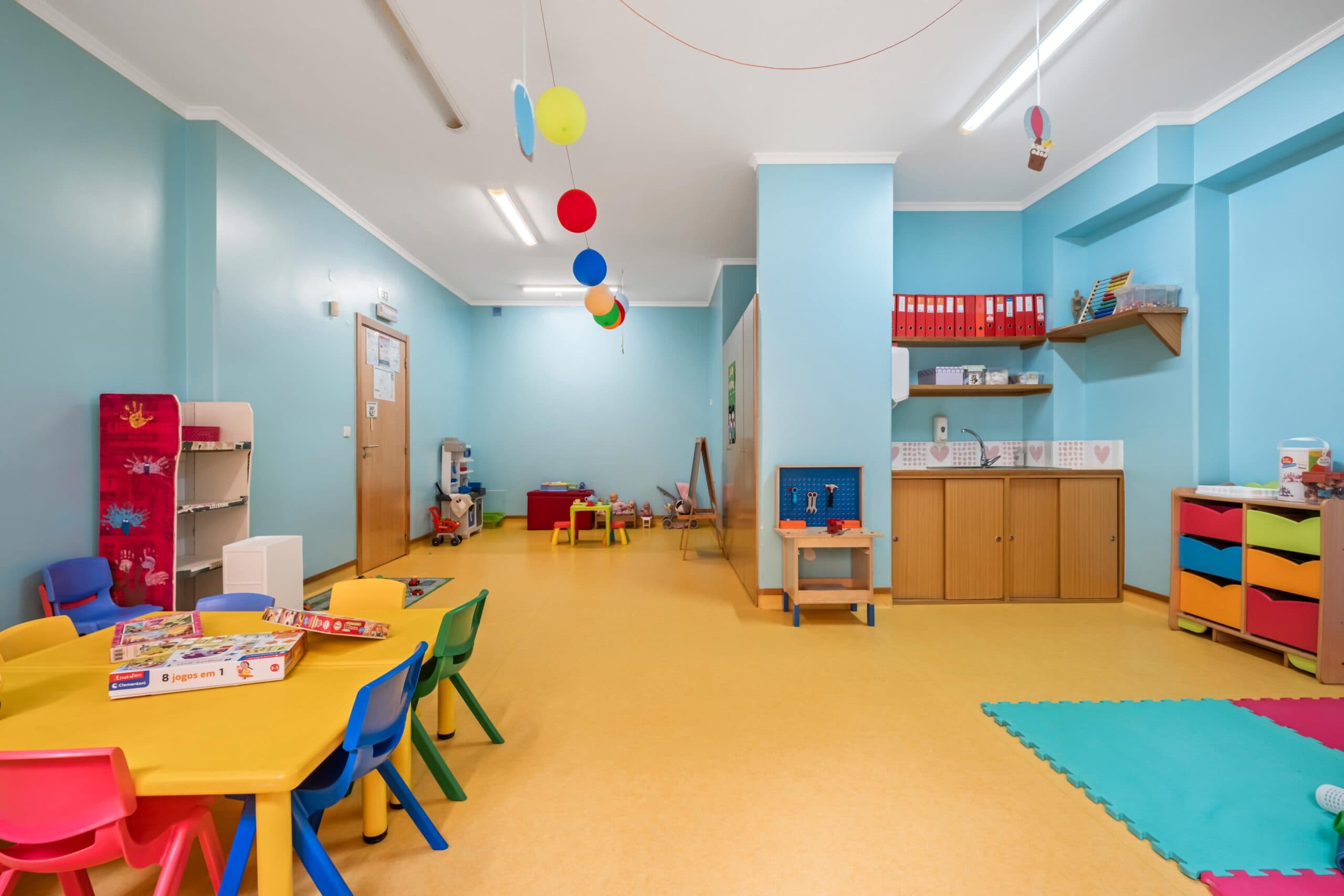 Sala jardim de infância Texugos com mesas, cadeiras, tapete e diversos brinquedos, no infantário A Toca dos Traquinas