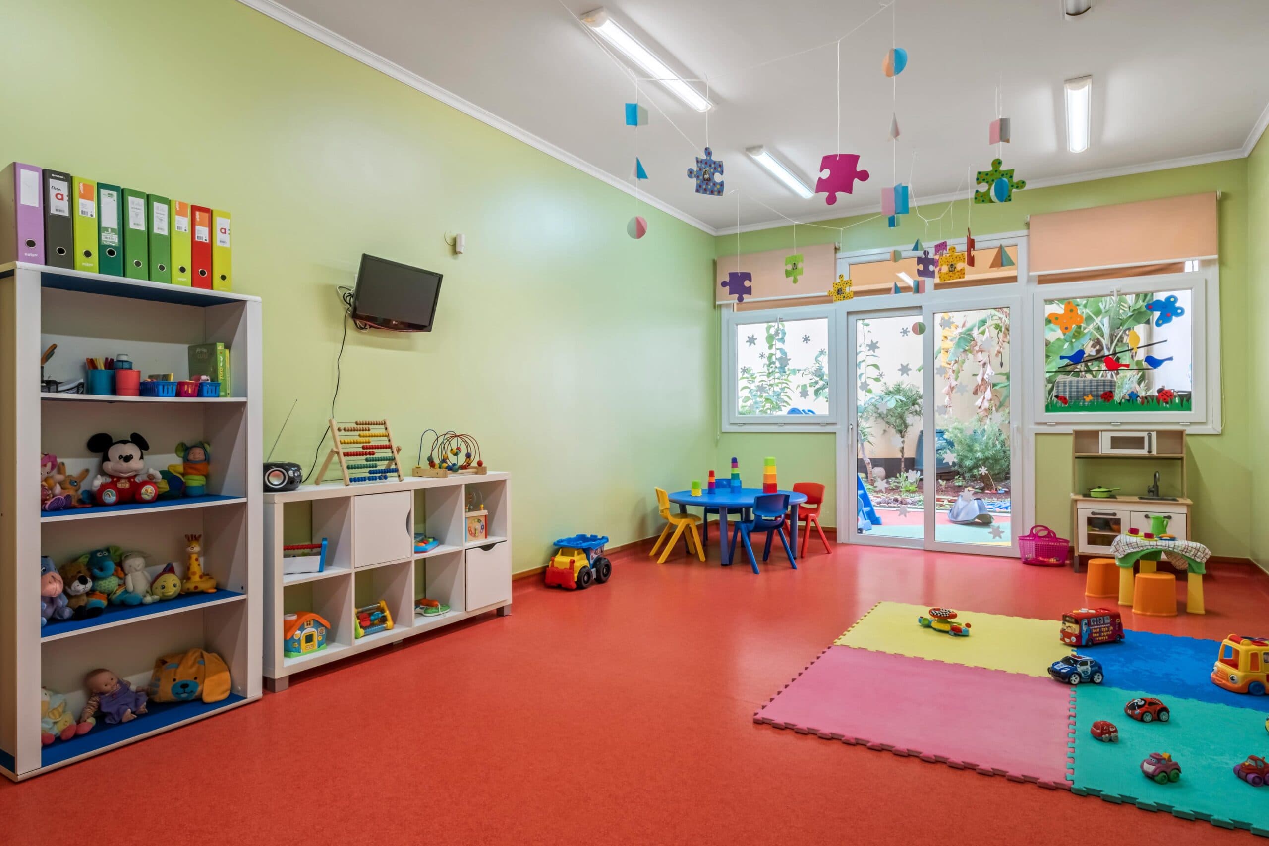 Sala transição Castores com mesas e cadeiras coloridas, e diversos brinquedos, no infantário A Toca dos Traquinas