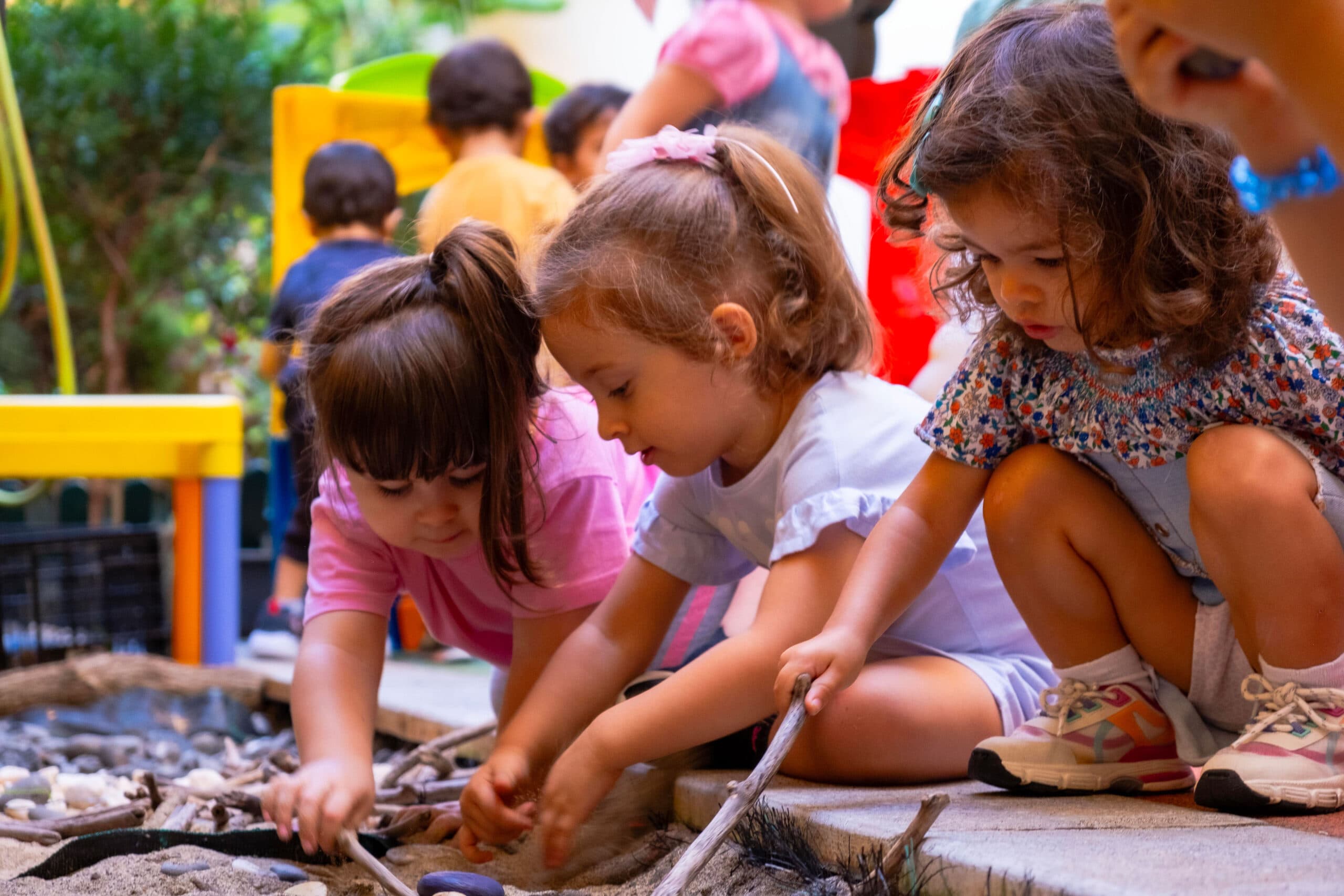 Três meninas a brincarem com diferentes texturas no parque do infantário A Toca dos Traquinas