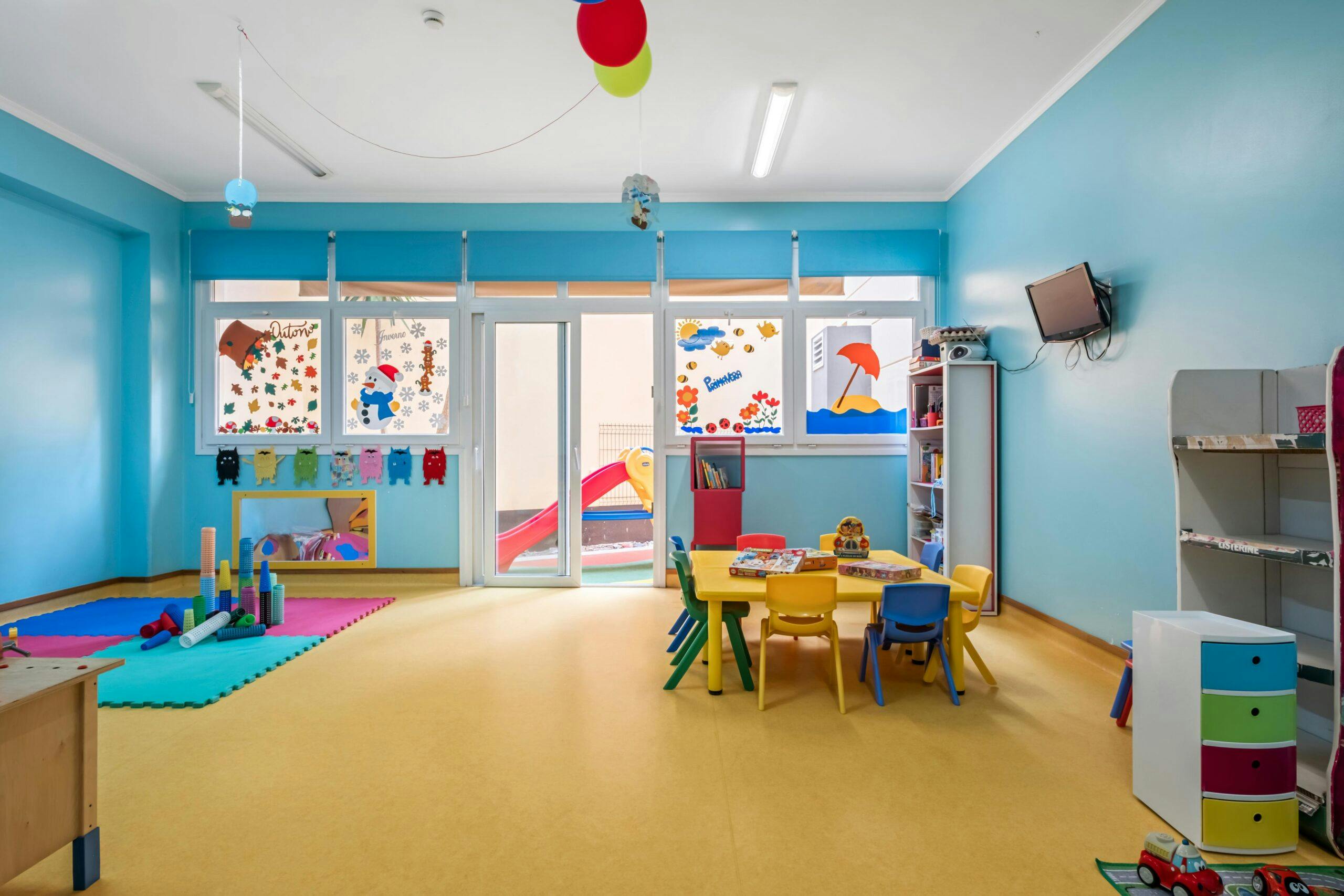 Sala jardim de infância Texugos com mesas, cadeiras, tapete e diversos brinquedos, no infantário A Toca dos Traquinas