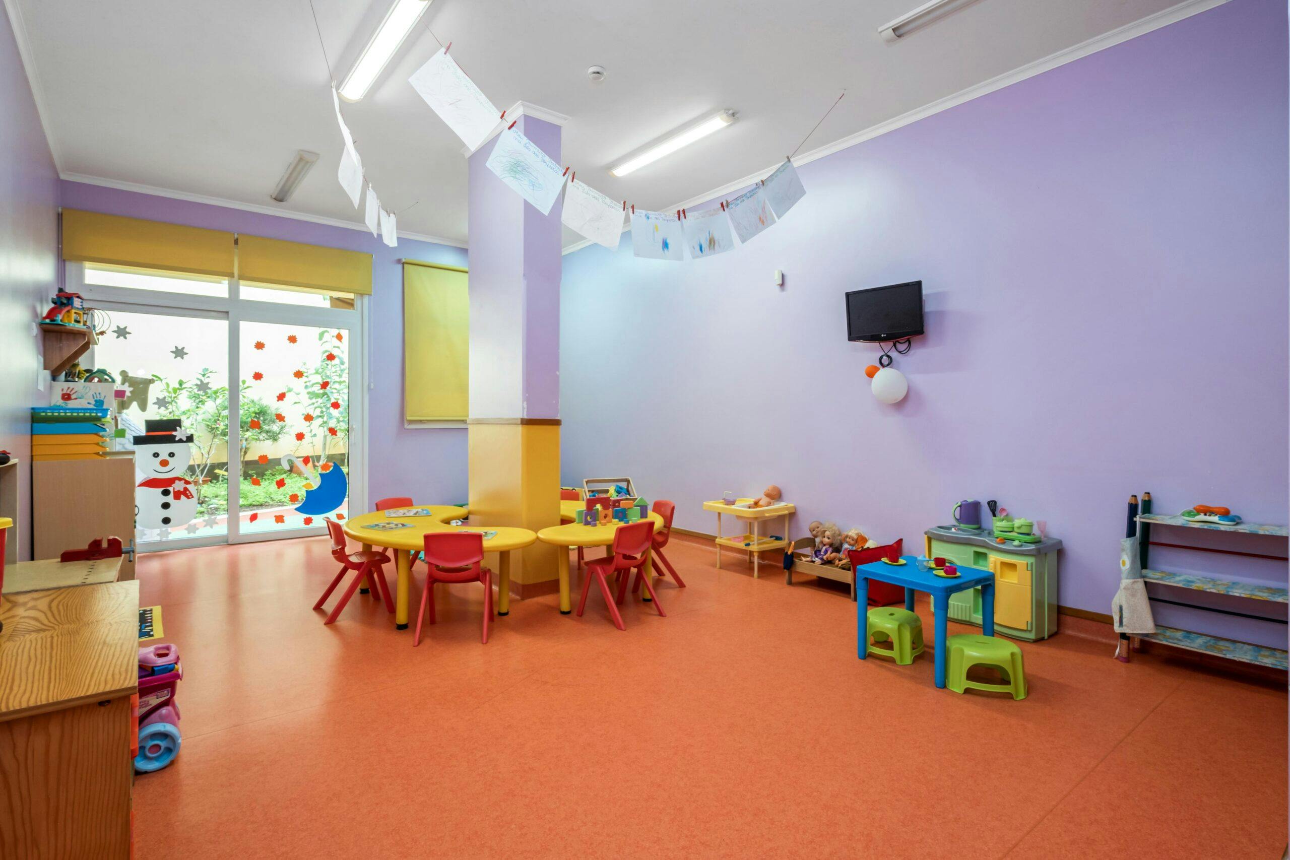 Sala transição Toupeiras com mesas amarelas, cadeiras vermelhas e diversos brinquedos, no infantário A Toca dos Traquinas