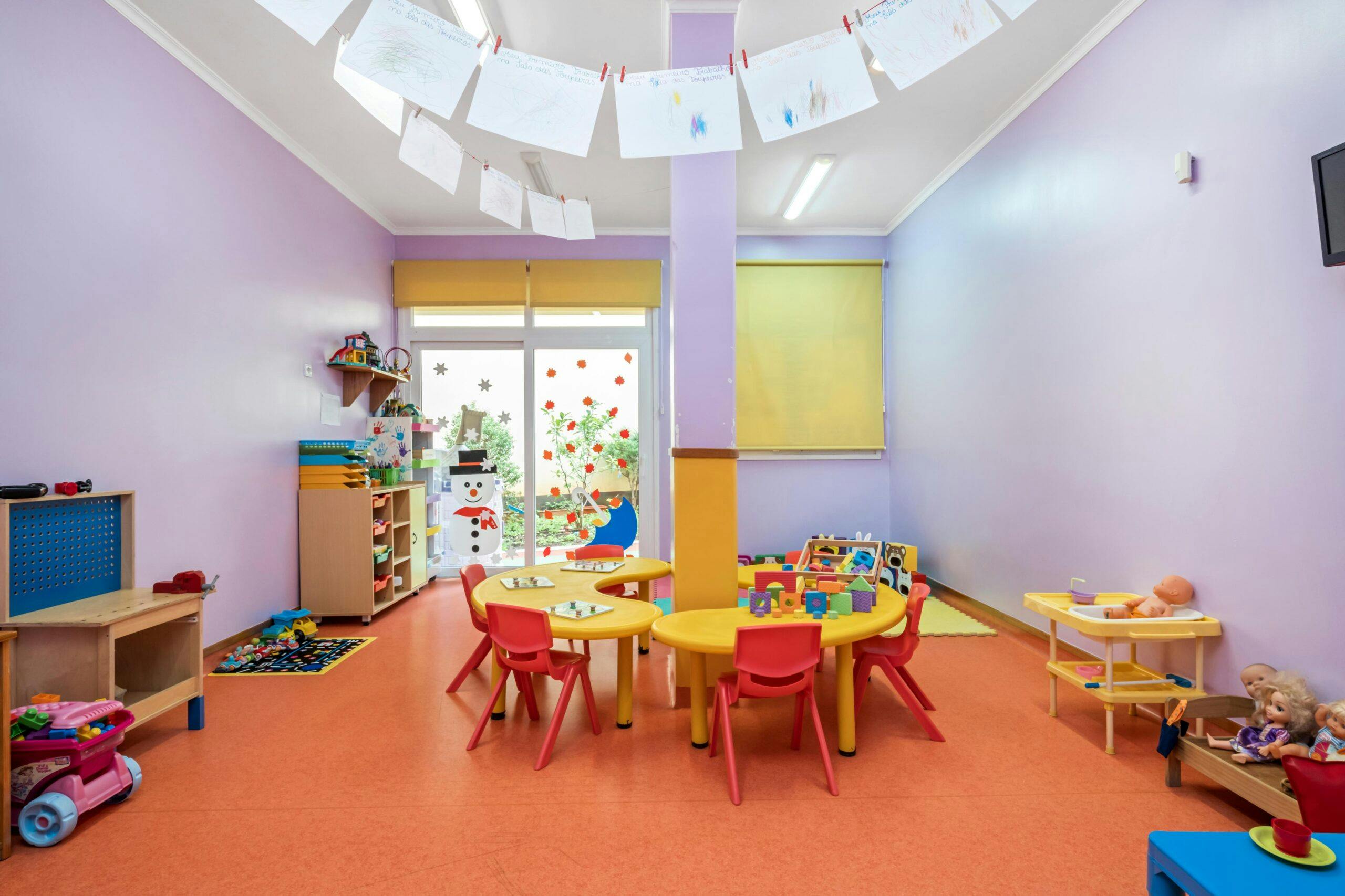 Sala transição Toupeiras com mesas amarelas, cadeiras vermelhas e diversos brinquedos, no infantário A Toca dos Traquinas