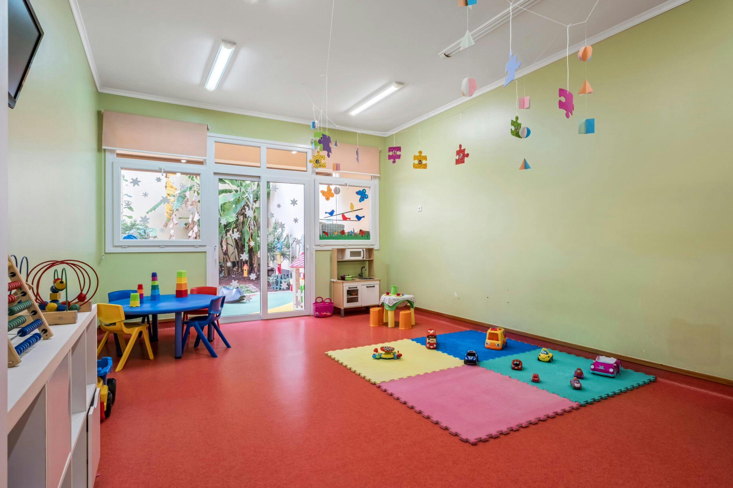 Sala transição Castores com mesas e cadeiras coloridas, e diversos brinquedos, no infantário A Toca dos Traquinas