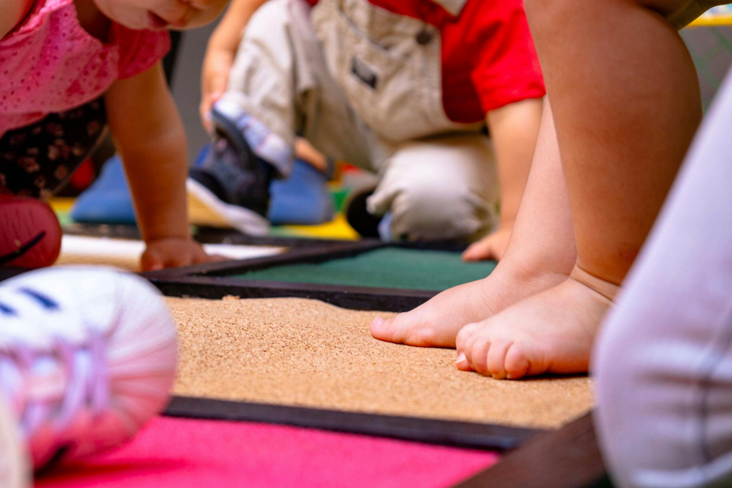 Crianças a tocar com as mãos e os pés em diferentes texturas, no infantário A Toca dos Traquinas